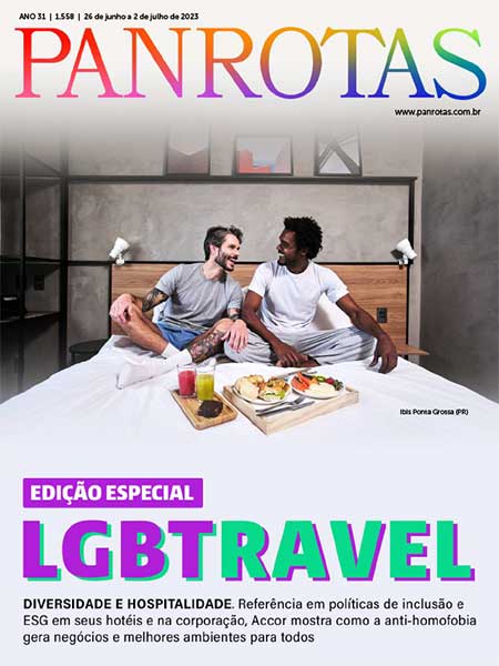 Capa da revista Panrotas, edição especial do Orgulho LGBT+, traz duas figuras masculinas na cama de um hotel. Um homem branco, de barba e tatuado, camiseta cinza e shorts azul. O outro homem é negro está usando uma camiseta branca e uma calça de moletom cinza. Ambos estão com as pernas cruzadas.